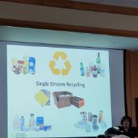 A woman demonstrates in front of a presentation about recycling
